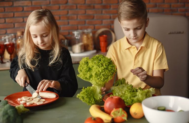 Focused little girl and boy sitting at desk with assorted vegetables and fruits while cooking in loft kitchen with brick wall