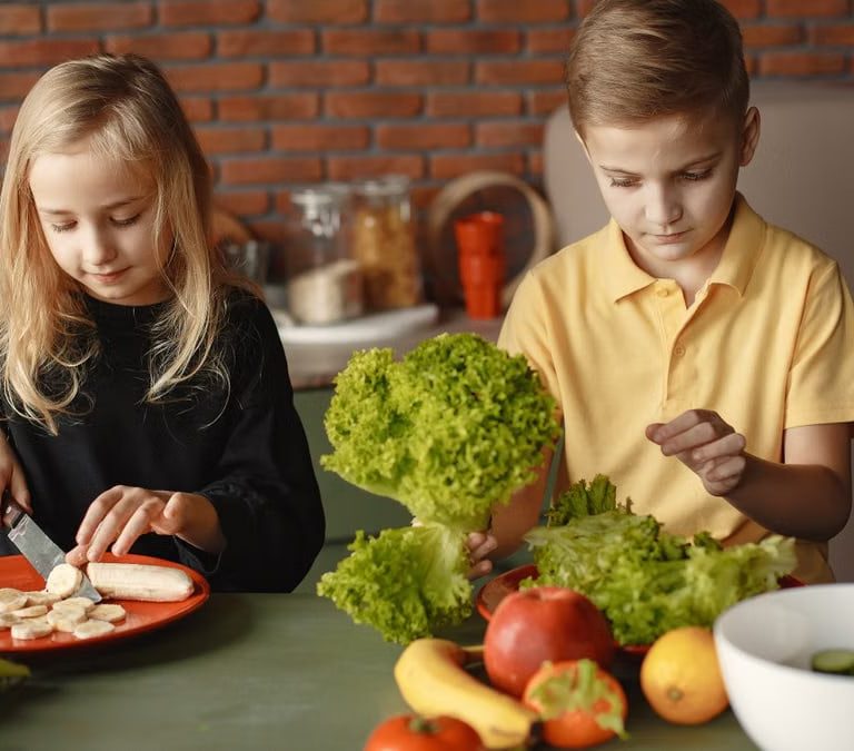 Focused little girl and boy sitting at desk with assorted vegetables and fruits while cooking in loft kitchen with brick wall