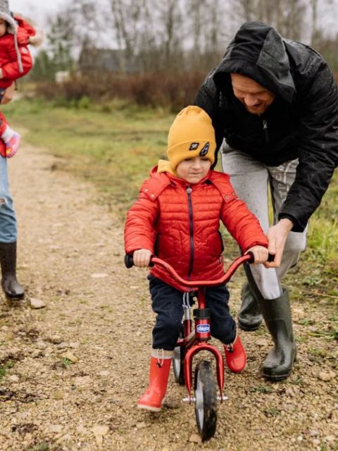 Happy family walking outdoors in fall, teaching child to ride bike.