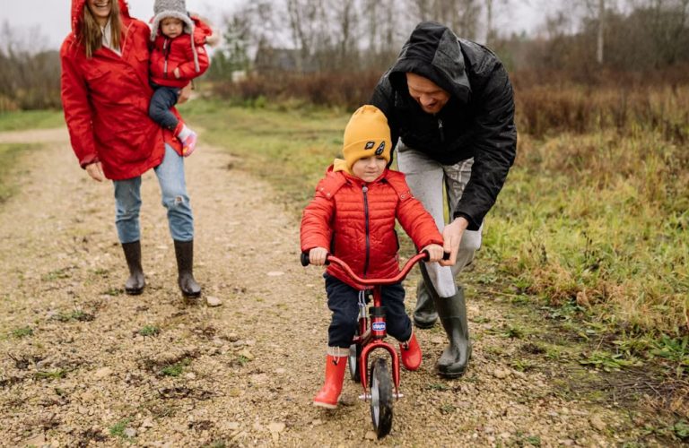Happy family walking outdoors in fall, teaching child to ride bike.